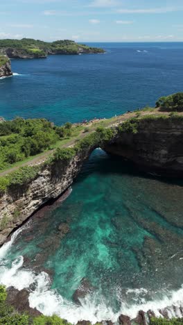 aerial establishing static of rocky arch and turquoise sea at broken beach and manta bay, nusa penida, bali at midday sun