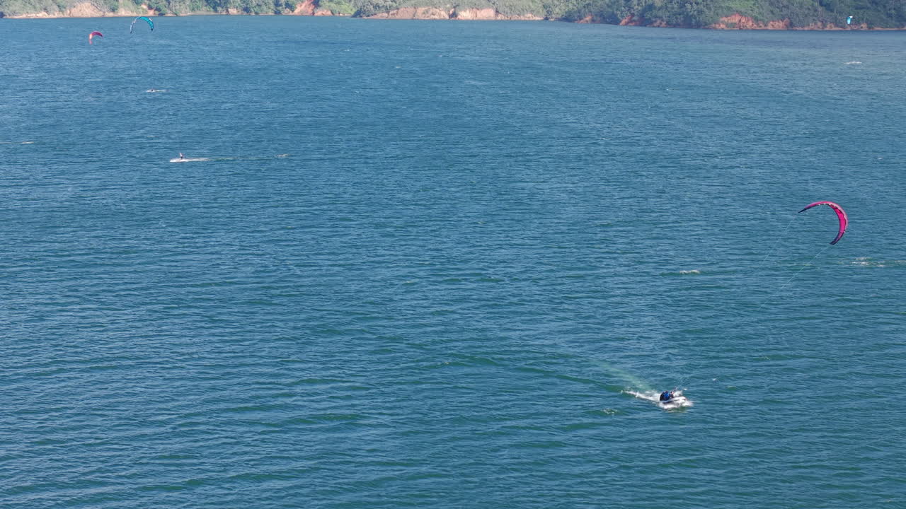Drone video captures vibrant kiteboarding on Lago Calima, revealing a dynamic interplay of vivid water hues and lush landscapes from above, evoking a thrill-seeking atmosphere