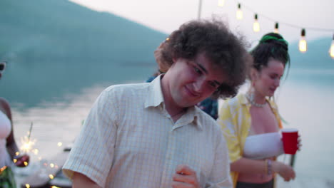 joven feliz bailando con sparkler en la fiesta del lago con amigos