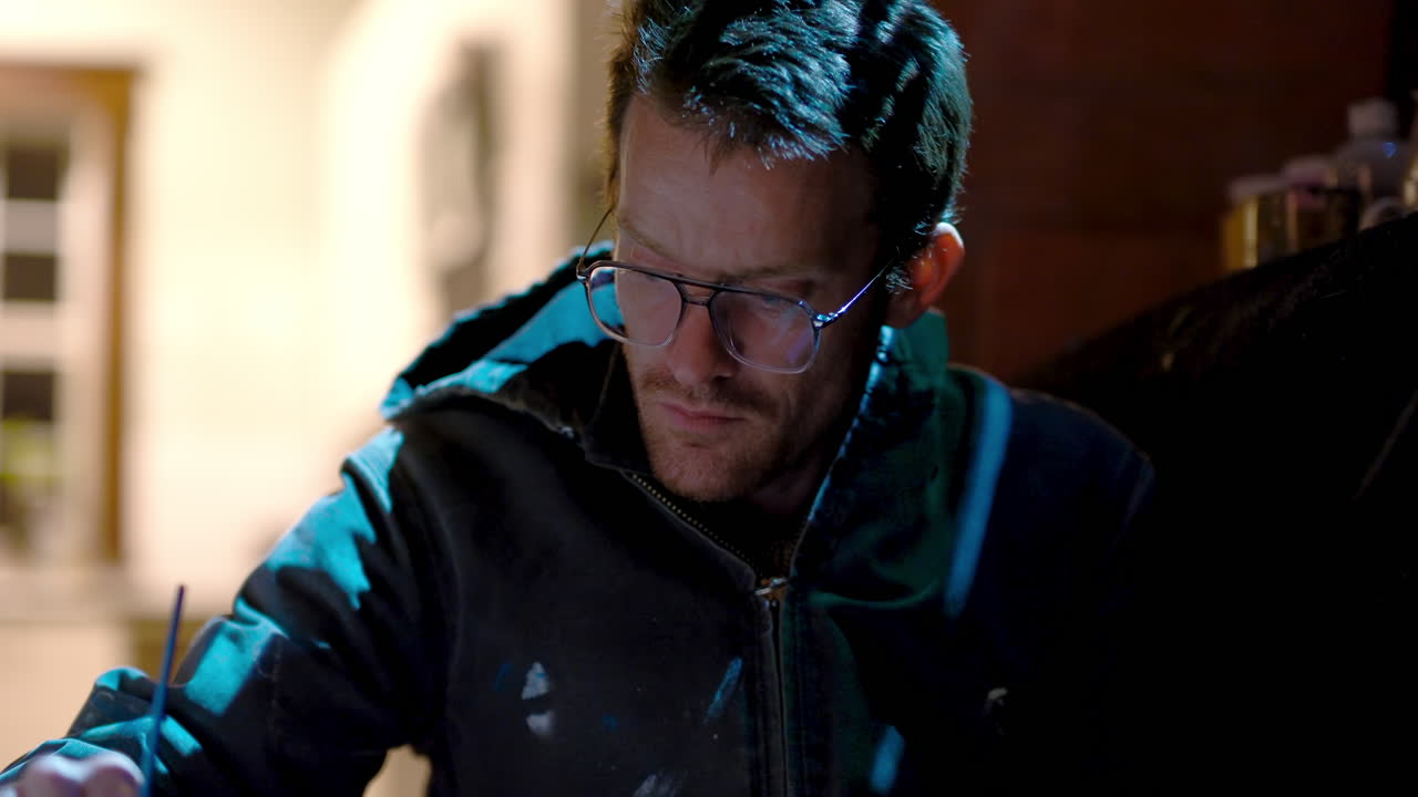 Close up of an artists face in the light of a projector as they paint