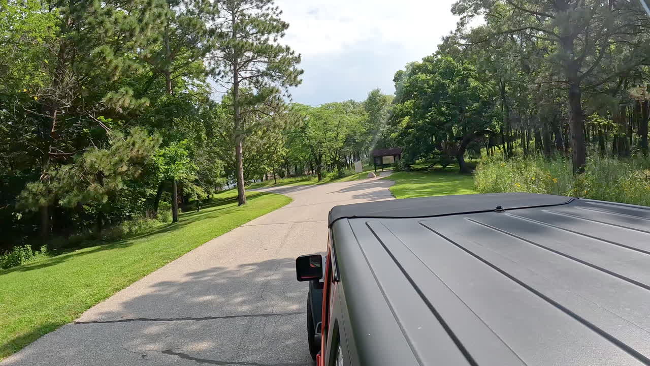 POV from vehicle roof - driving on paved road in county park through a wooded area towards the Des Moines River in central Iowa on a sunny, summer day; vacation, holiday or recreation