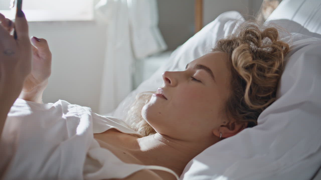 Young adult using smartphone in bed closeup. Girl resting in peaceful morning