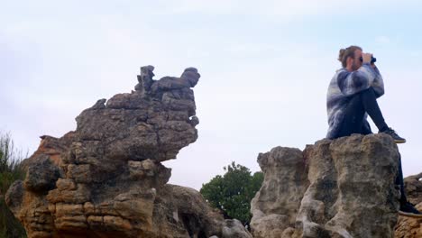 man sitting on rock looking through binoculars 4k