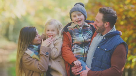 Portrait-Of-Family-With-Mature-Parents-Carrying-Two-Children-In-Front-Of-Autumn-Leaves