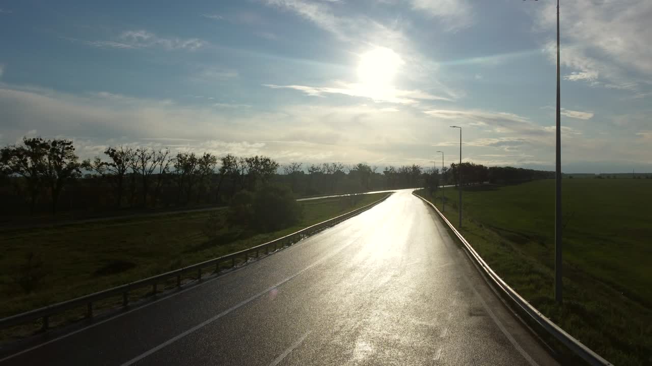 Drone rises above wet asphalt road for cars between sown fields in spring morning.