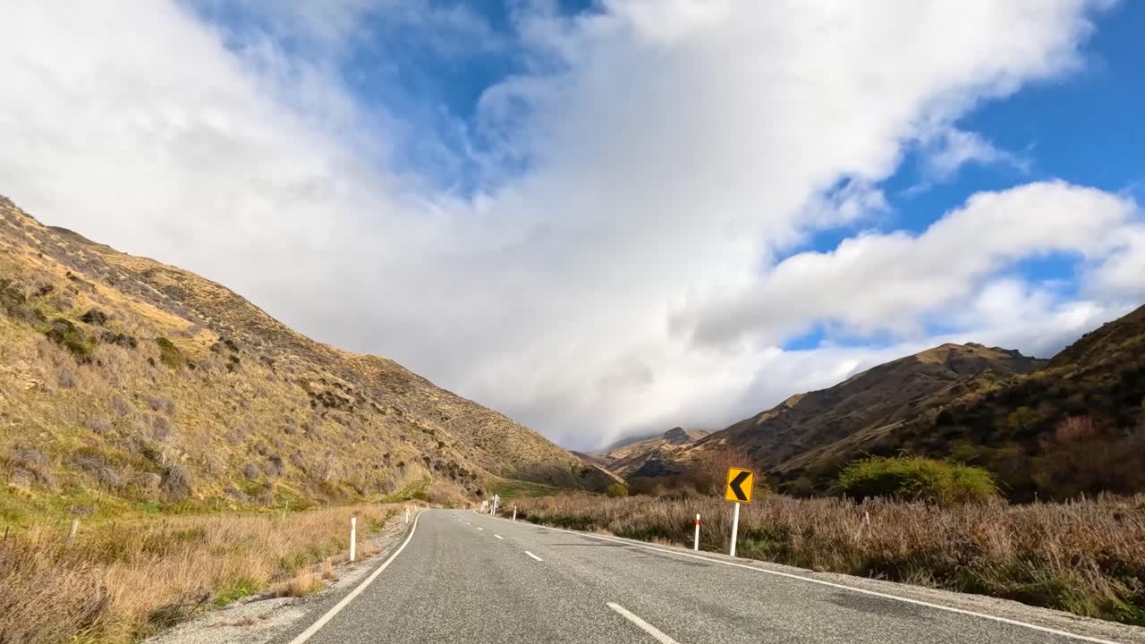 A serene drive through Wanaka's winding roads, showcasing lush hills and expansive skies under soft natural lighting