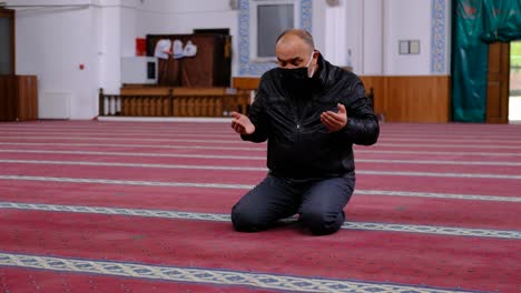 old man wearing mask raising his hands and praying in the mosque