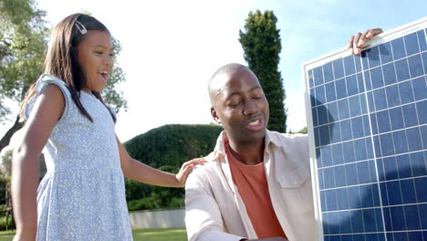 holding solar panel in backyard, smiling father and daughter promoting renewable energy