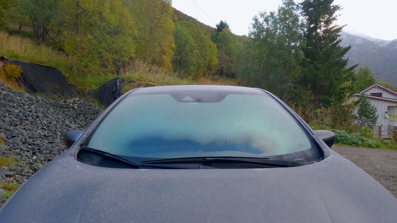 Defrost the car windshield on a Nissan Leaf EV Car during autumn in Northern Scandinavia inside the Arctic polar Circle. The sky is reflecting on the Window