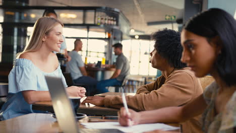 woman working on laptop in foreground with couple meeting socially behind in busy coffee shop