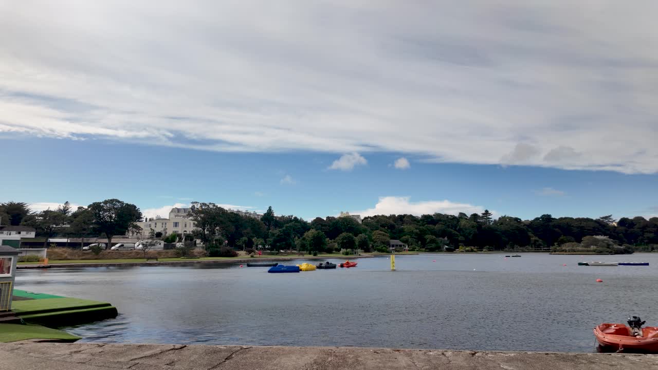 Mooragh Park lake on the Isle of Man with colorful pedal boats and waterfront buildings under a blue sky