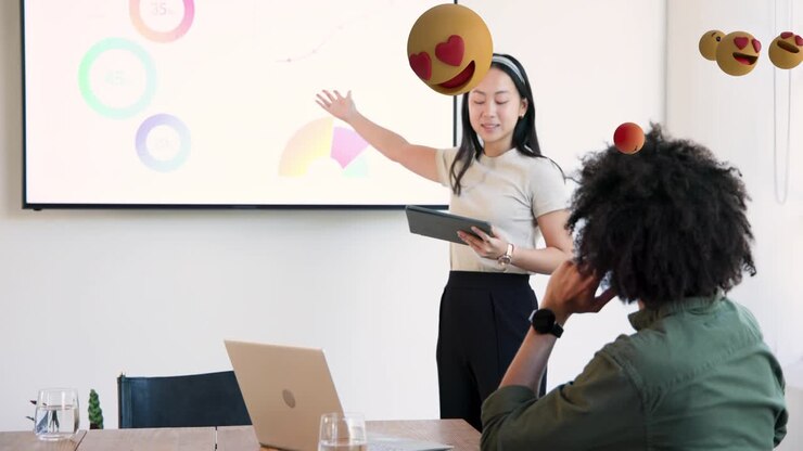 Donna che utilizza un tablet ed è in piedi per una demo, creando una sovrapposizione di emoji mentre indica dei grafici aziendali