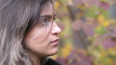 brunette girl in autumn forest stands near yellow and red leafs and looks sideways - close shot