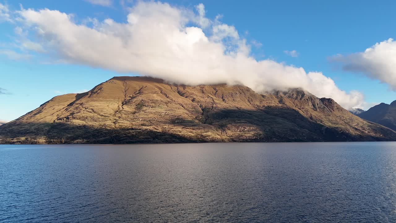 A tranquil scene of a mountain and lake under a bright blue sky with scattered clouds