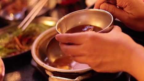 hand serving korean soup into a bowl