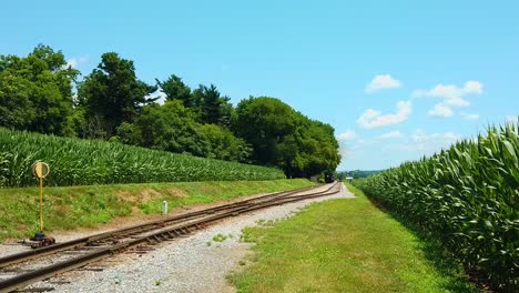 Schöner-Sonniger-Tag-Mit-Maisfeldern,-Blauem-Himmel-Und-Wenigen-Wolken-Und-Einer-Antiken-Dampflokomotive,-Die-Sich-Nähert