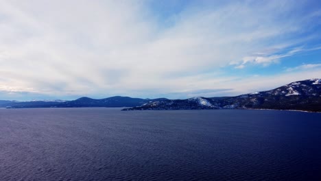 Aerial-drone-shot,-view-over-the-crystal-clear-lake-while-slowly-descending-in-the-woods-at-Lake-Tahoe,-Nevada-California