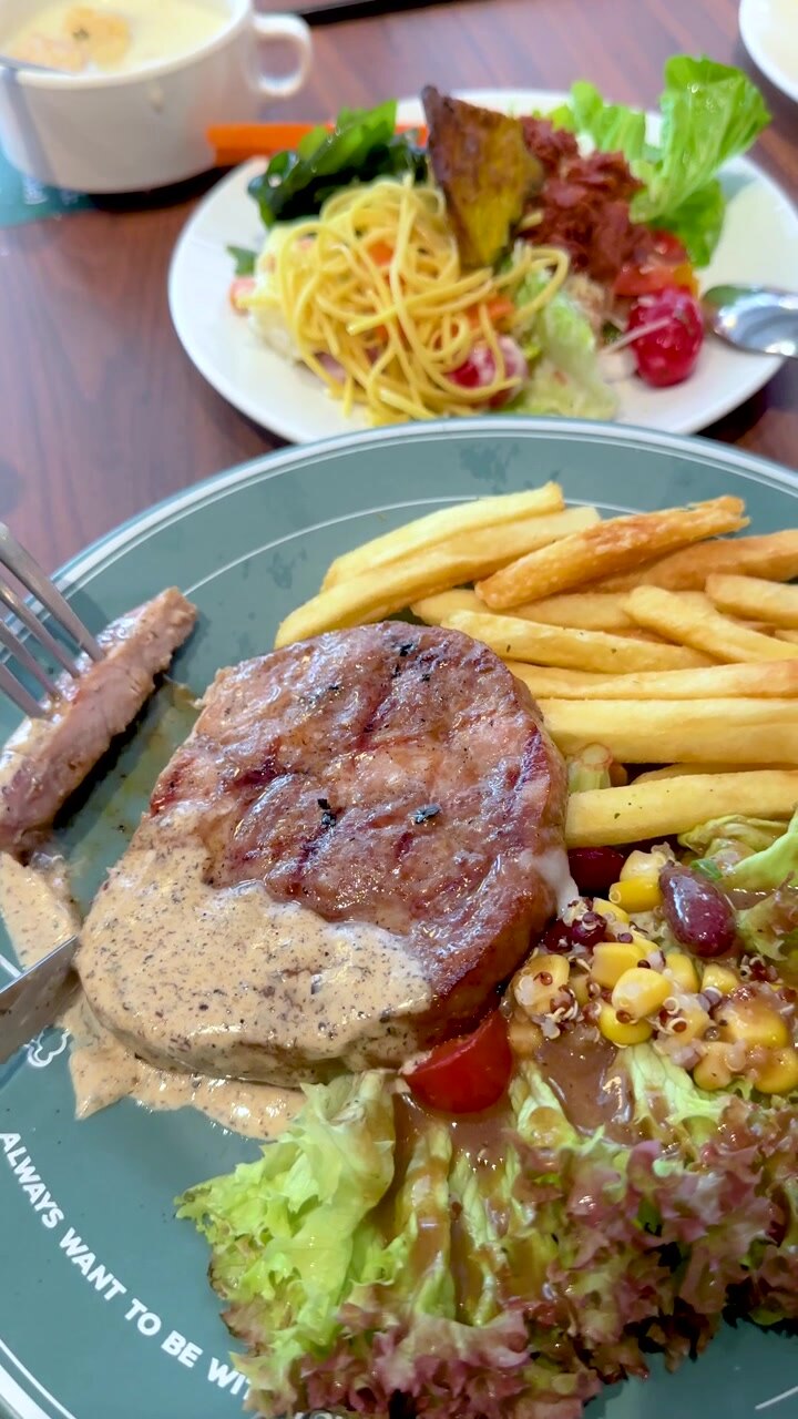 Una persona usa un cuchillo y un tenedor para cortar un filete de cerdo a la parrilla servido con patatas fritas.