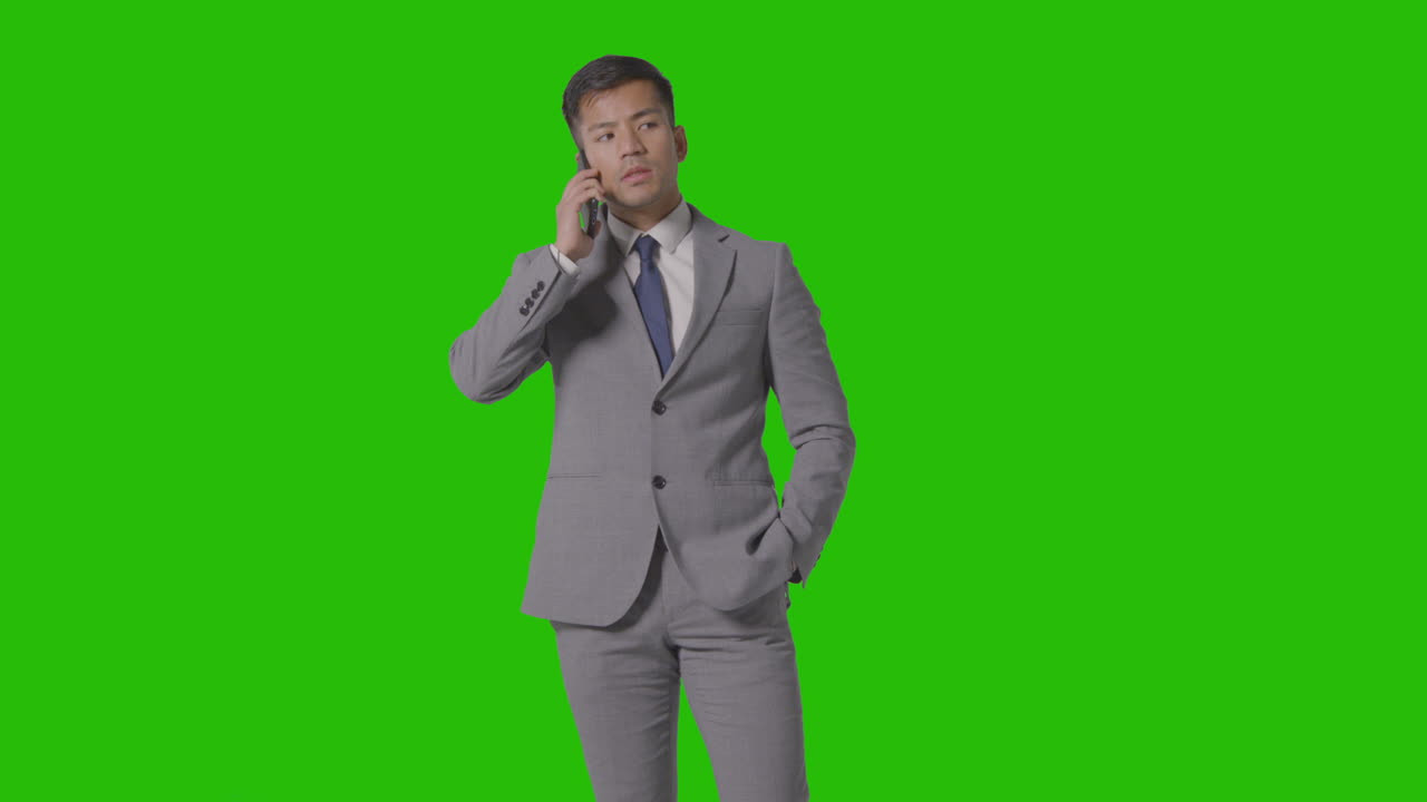 녹색 화면에 대해 휴대 전화로 이야기하는 정장을 입은 사업가의 3/4 길이 스튜디오 샷
