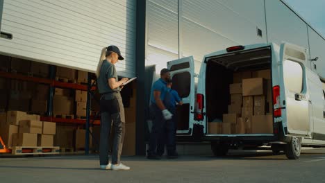 outside of logistics distributions warehouse delivery truck: manager using tablet computer, workers start unloading cardboard boxes, online orders, purchases, e-commerce goods. pan wide shot