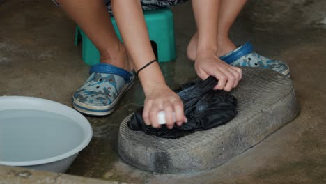 las manos de una mujer norcoreana fregando y lavando la ropa con jabón en una tabla de lavado de piedra fuera de la casa en un pueblo de estilo antiguo - de cerca