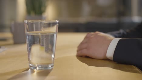 nahaufnahme zeigt die hände eines männlichen kandidaten, der im büro für eine stelle interviewt wird, mit einem glas wasser