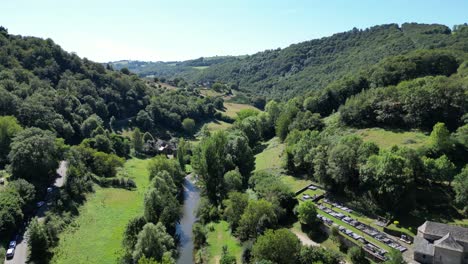 drone aerial view in france countryside flying over a green valley with a small river, green trees on a sunny day in belcastel