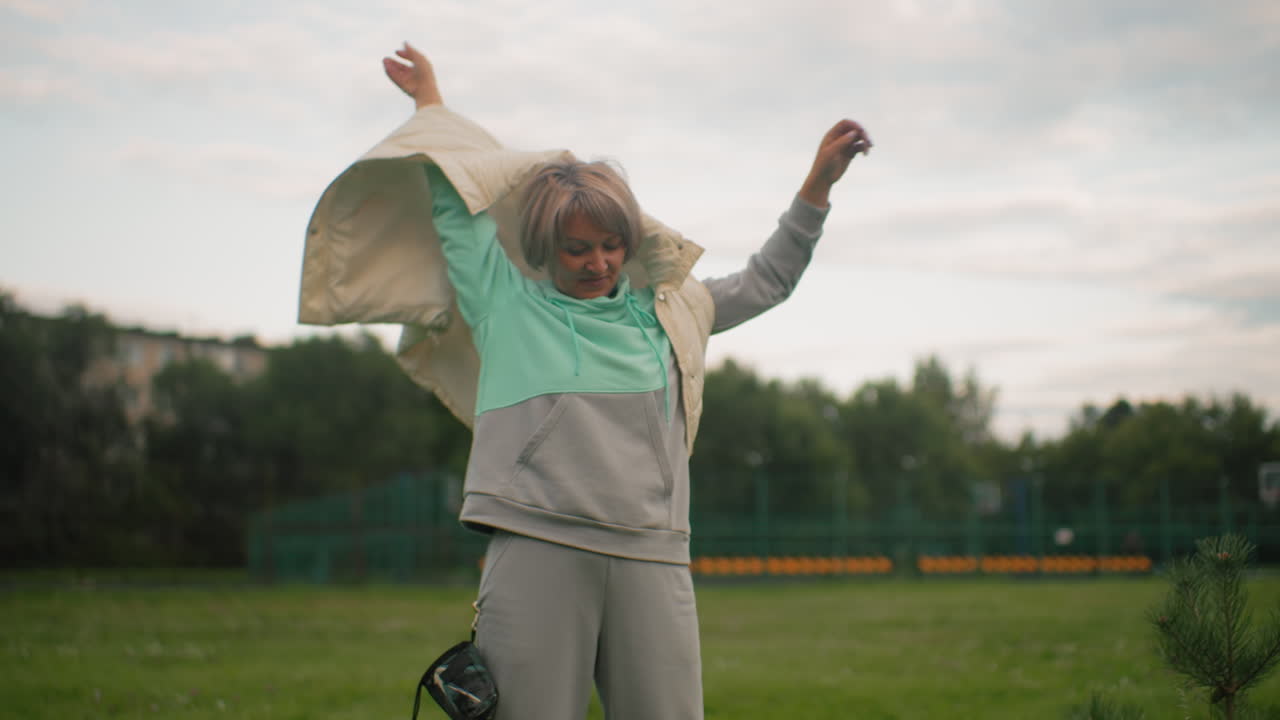 Close up shot of trainer putting on her coat after a training session in an outdoor field. She is ready to continue the day as her dog looks around in the background, enjoying the environment