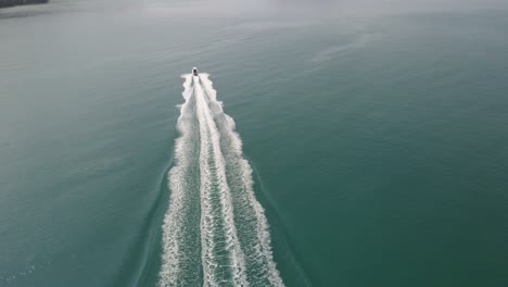 Aerial-drone-static-shot-of-a-speed-boat-traveling-fast-towards-an-Island-in-a-tropical-sea-with-mountain-coastline