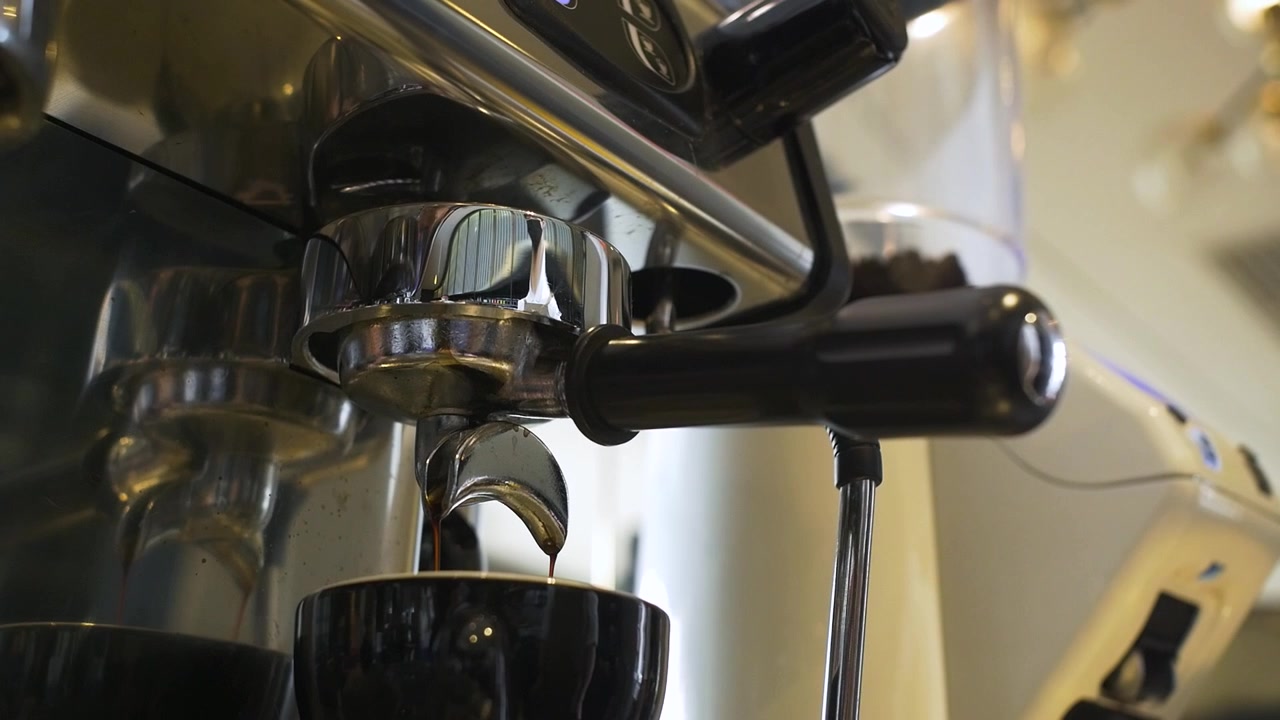 Il barista blocca il portafiltro sulla macchina da caffè espresso e posiziona la tazza sotto prima che il caffè caldo goccioli. Vista ravvicinata di un lavoratore che prepara un caffè espresso