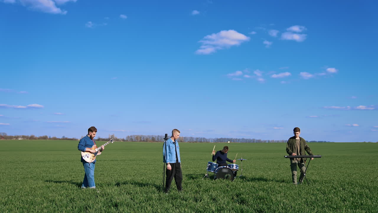 Young musical band giving a concert on field. Friends perform music with musical instruments under blue sky. Outdoor entertainment.