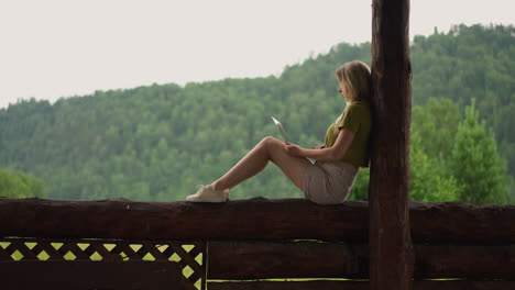 Woman-programmer-works-on-laptop-sitting-on-rustic-fence