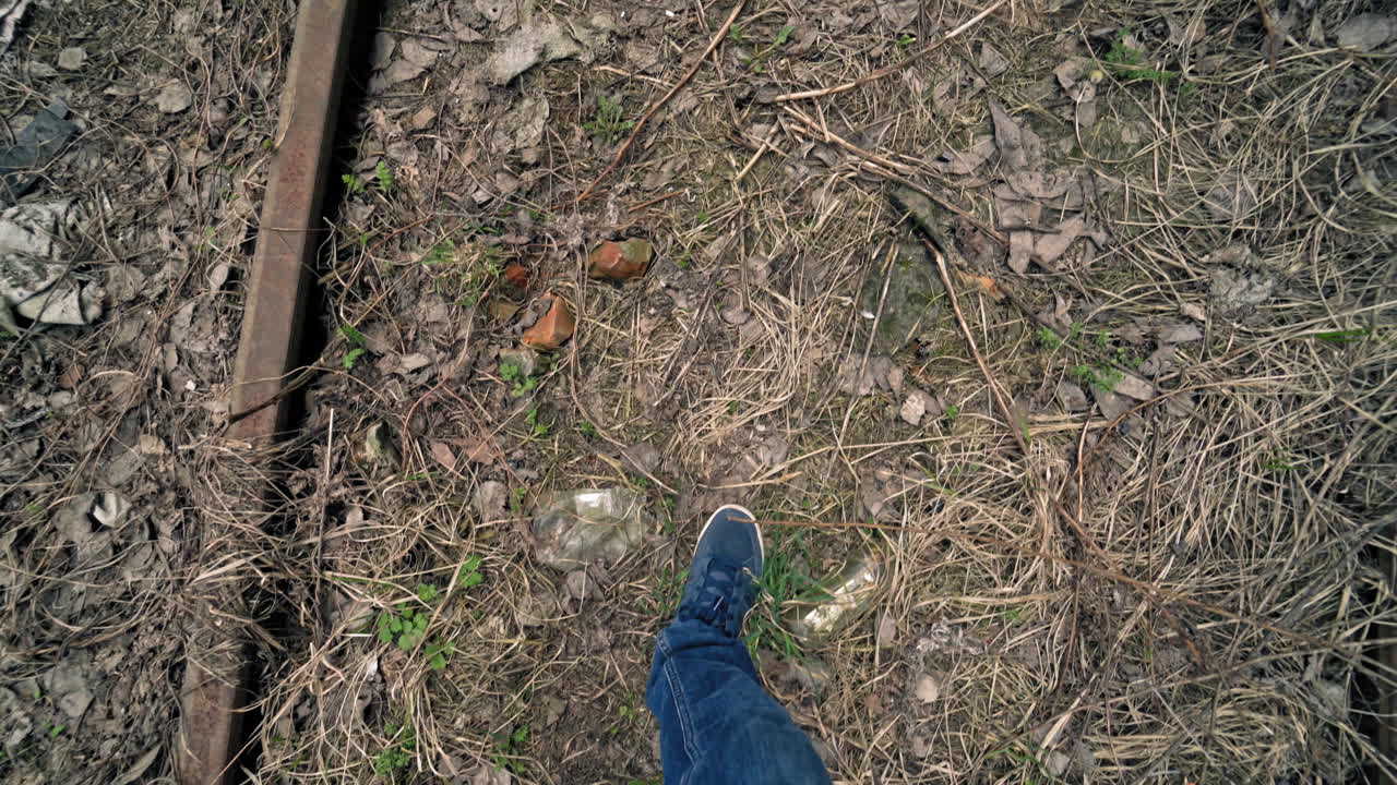 Man's legs walking on the dirty ground with many garbage outdoors. Male's feet stepping along the dirty place with glass bottles and rubbish.