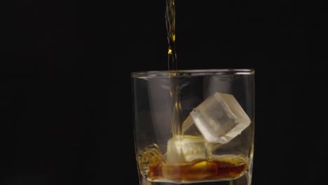 alcohol being poured in a glass with with ice cubes