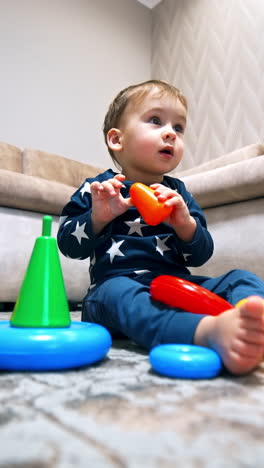 caucasian toddler plays with bright pyramid on the floor. playtime for a baby boy at home. low angle view. vertical video