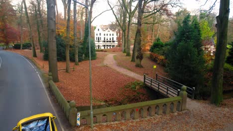 AERIAL---Yellow-car-approaching-Staverden-Castle,-Veluwe,-Netherlands