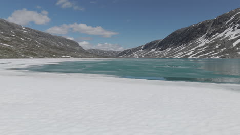 slowmotion drone shot flying close over the ice flakes on langvatnet lake in norway close to the strynefjellsveg on a sunny day surrounded by shiny rocks and mountains log