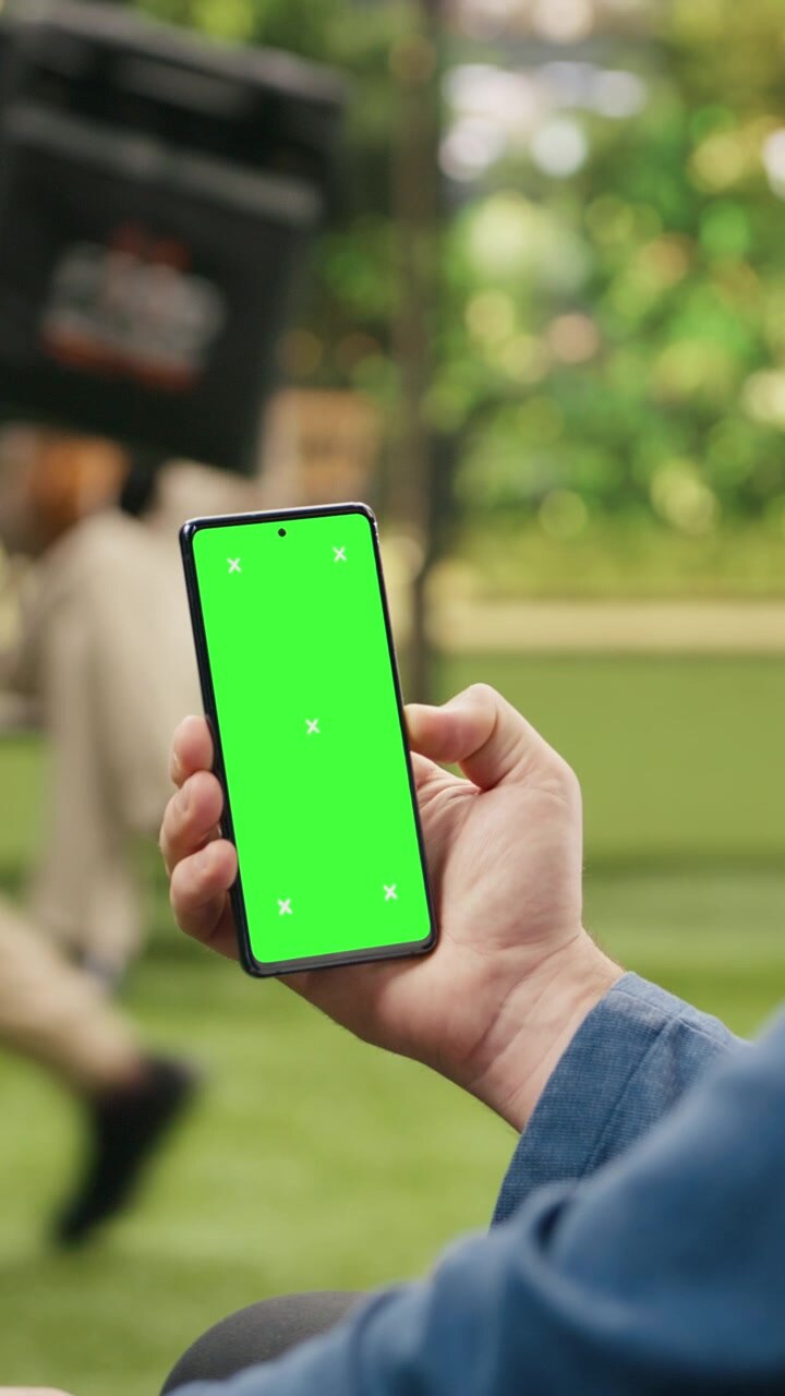 Mockup pubblicitario per smartphone con video verticale che utilizza un green screen verticale mentre un uomo lo tiene all'aperto