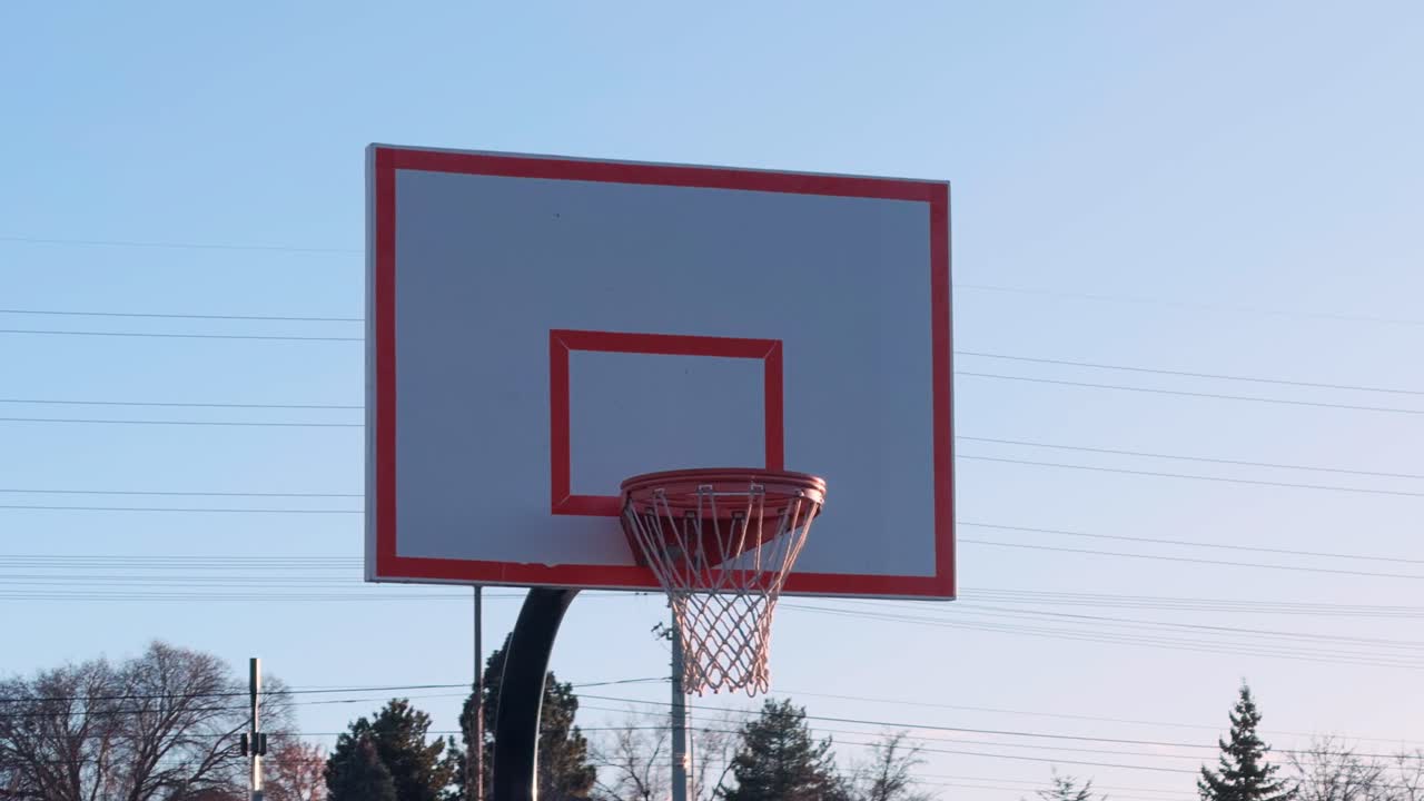 Lenta panoramica di un canestro da basket all'aperto e di un tabellone con un cielo azzurro limpido