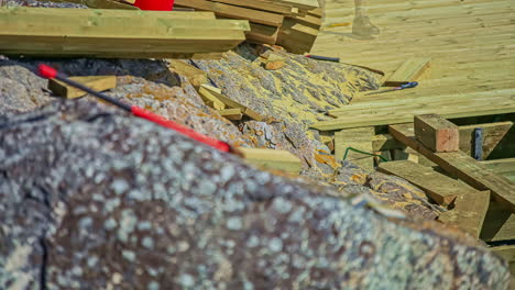 static shot of a worker constructing wooden pier on a rocky shore in timelapse