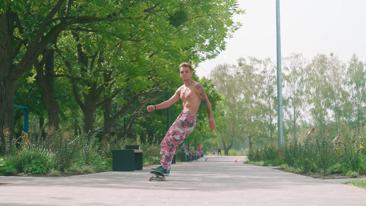 Young Man Skateboarding Shirtless on Paved Path in Green Park