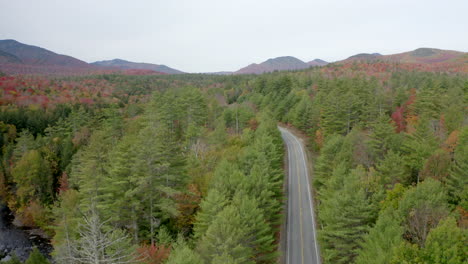 vista aérea de aumento lento de una carretera vacía que atraviesa un vasto bosque en las montañas adirondack con vibrantes colores de otoño