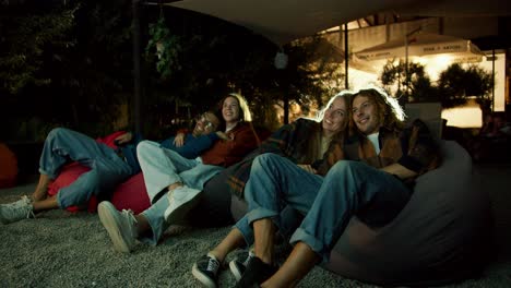 Two-couples-in-love-are-sitting-on-beanbag-chairs-and-watching-a-movie.-A-party-outside-the-city.-Rest-in-the-country-house