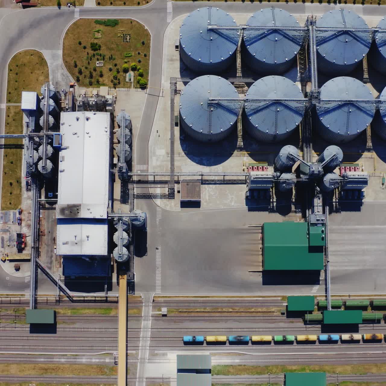 Grain silos. Aluminum containers for storage harvest. Railway with freight trains on industrial territory. Silver grain terminals on field. Top view. Agribusiness concept.