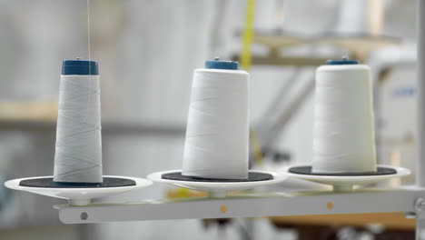 Closeup-of-three-big-bobbins-with-thin-white-thread-on-working-professional-sewing-machine.-Real-time-full-hd-video-footage