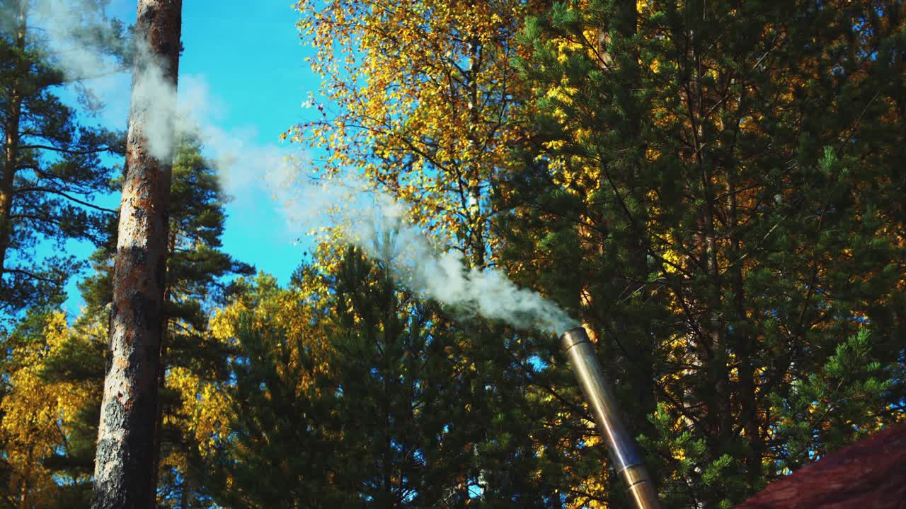 Small angled chimney belches smoke during autumn forest camping