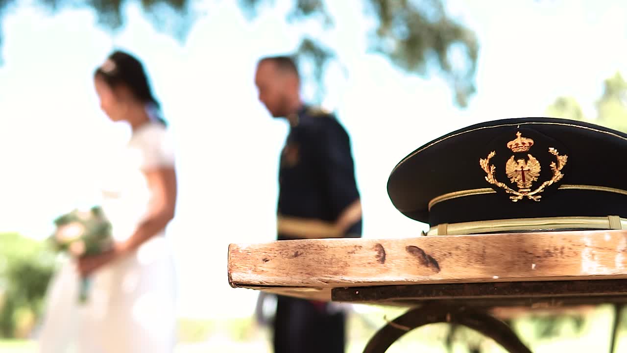 Cappello militare in primo piano e un matrimonio sfocato sullo sfondo.