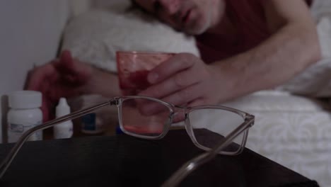 sleepy adult male drinking a glass of water in bed