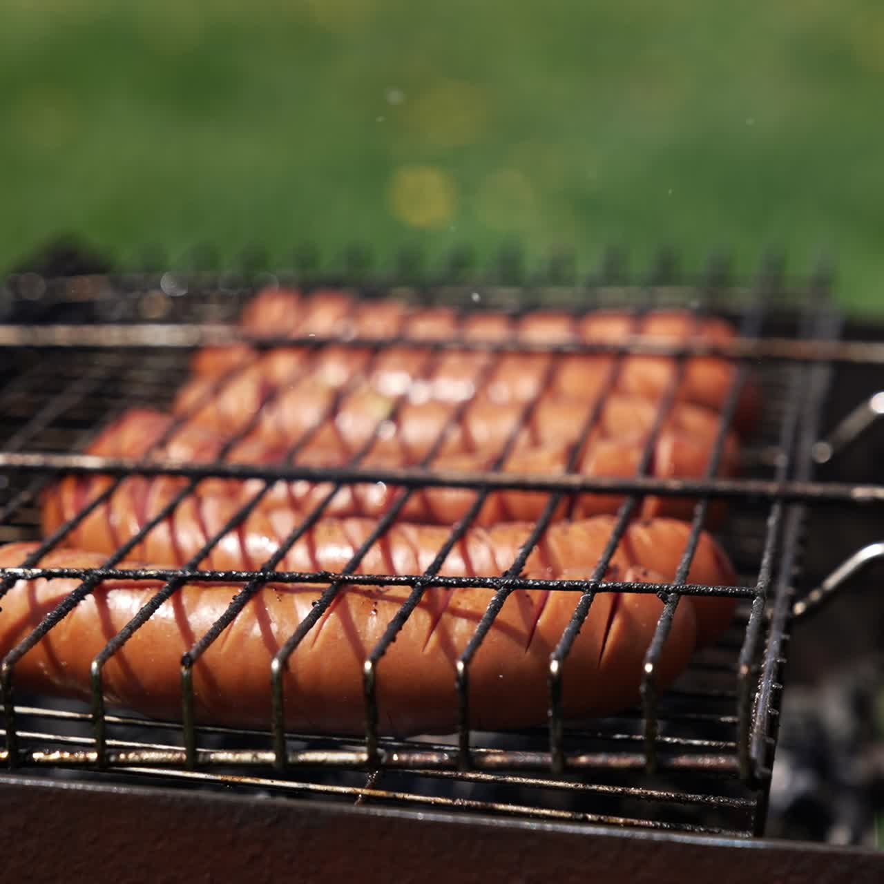 Roasting sausages in smoke. Juicy meat sausages cooking on a grill plate outdoors. Grilling food during summer vacation. Close-up