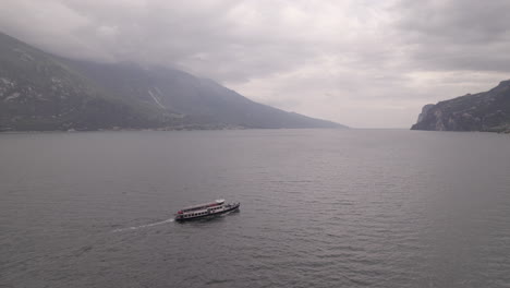 Drohnenaufnahme-Einer-Fähre,-Die-An-Einem-Grauen-Tag-Mit-Bergen-Und-Stausee-In-Die-Italienische-Stadt-Limone-Am-Gardasee-Fährt